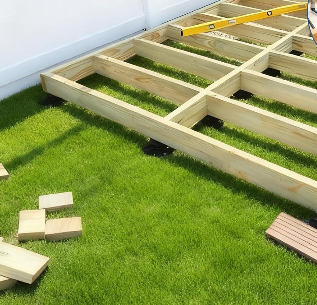A timber deck frame on a lawn, supported on black adjustable pedestals